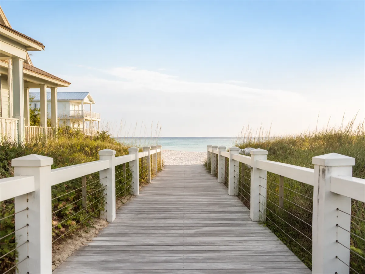 A white-railed boardwalk running through dune grass to the sand, the ocean beyond